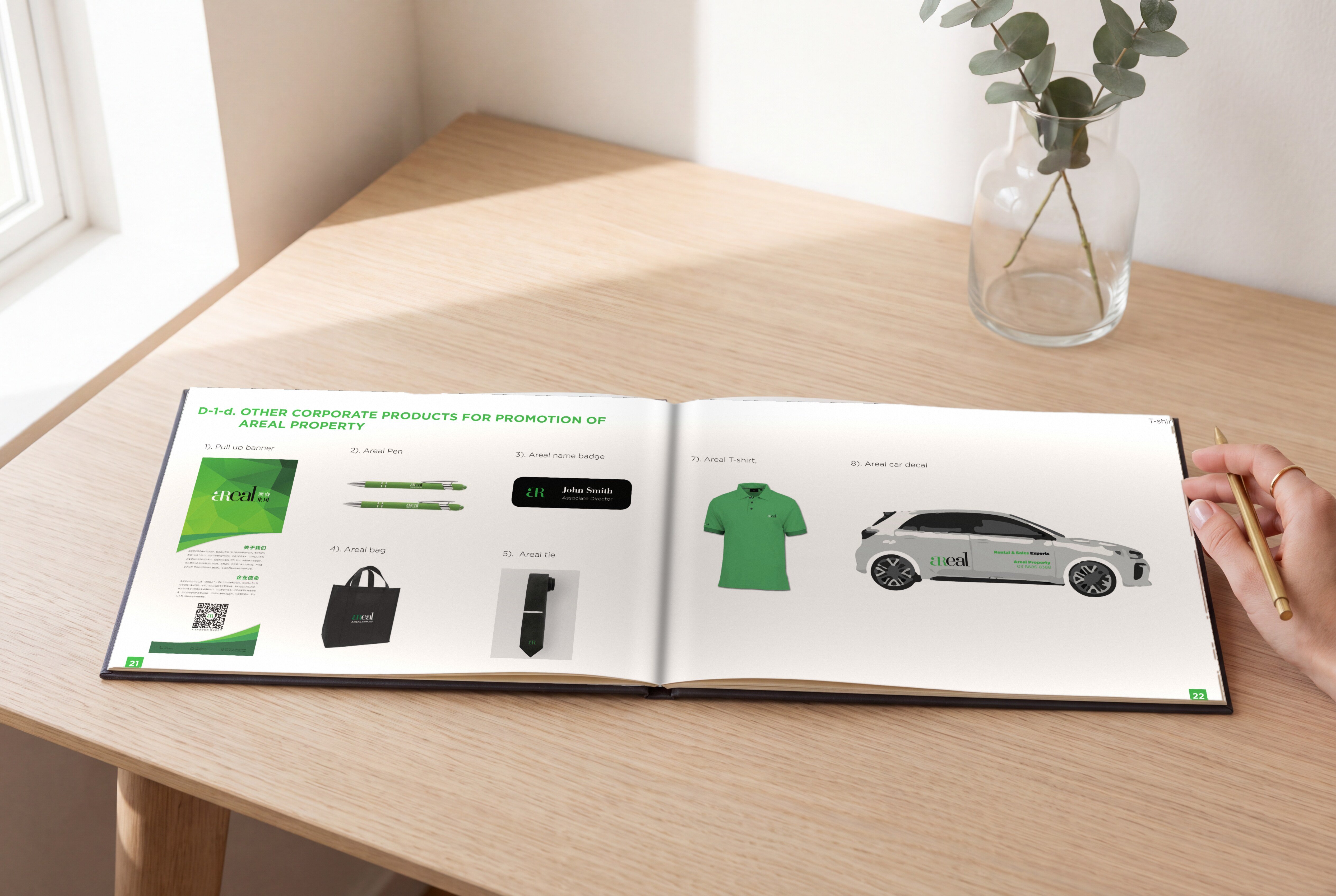 Brochure open on an oak desk at Areal's other corporate products, from a pull-up banner, pens and a name badge to a bag, a tie, a polo shirt and a car decal, a woman's hand holding a pen at the page edge