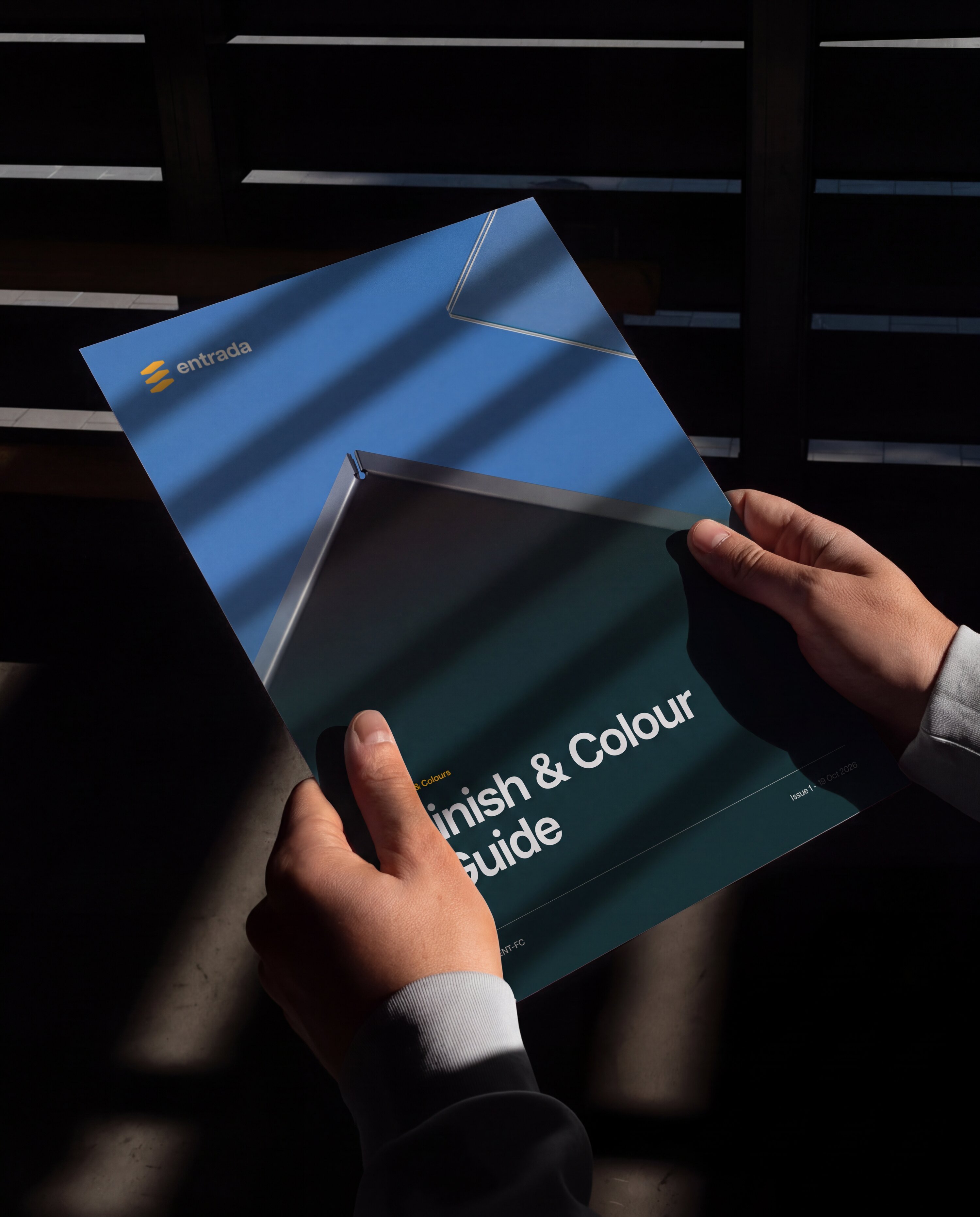 Hands holding the Entrada Finish and Colour Guide, its cover a canopy against blue sky