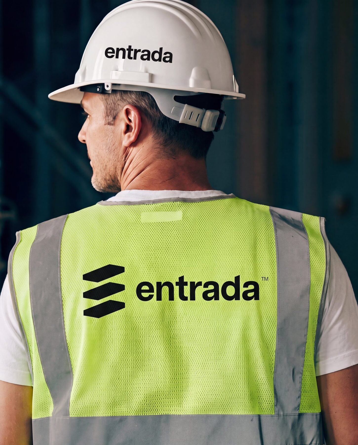 Entrada logo on the back of a hi-vis vest, with the wordmark on a white hard hat