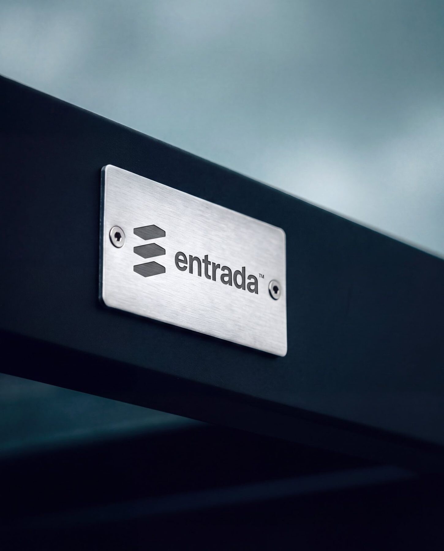 Entrada mark and wordmark engraved on a brushed metal plate fixed to a dark canopy beam