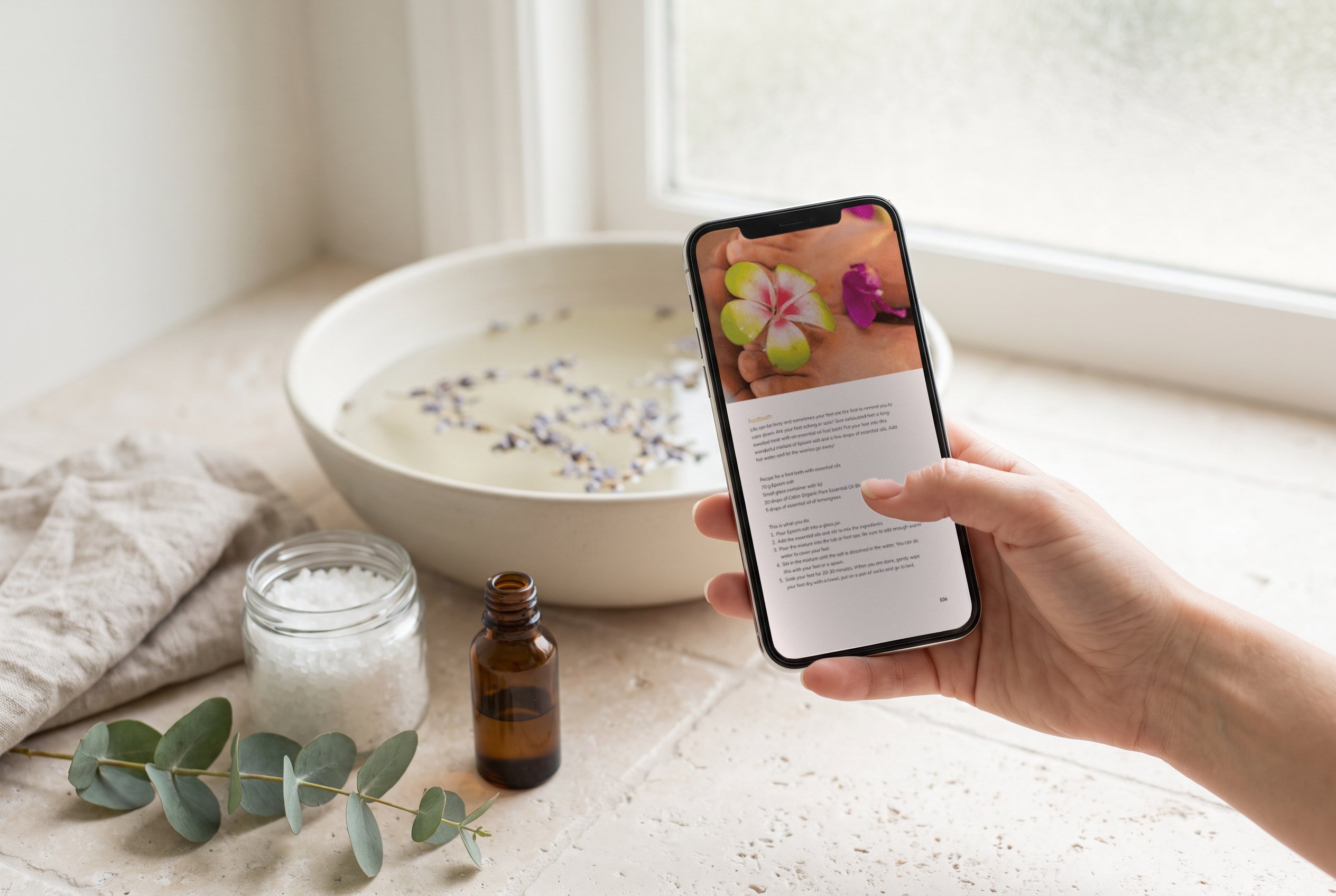 The ebook's footbath page on a phone held in a woman's hand above a bowl of water with lavender