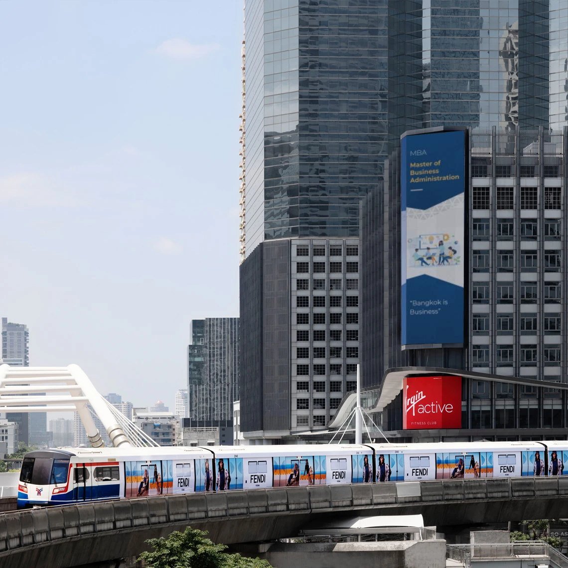 The MBA ad on a tall LED screen among Bangkok towers, above a passing skytrain